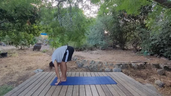 תנוחת כפיפה קדימה בעמידה – אוטנאסנה בר עומד על מזרן ומתקפל לפנים כשהידיים נוגעות ברגליים בתנוחת אוטנאסנה.