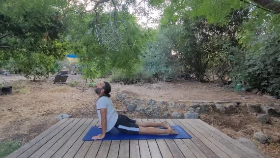 בוג'נגאסנה – תנוחת קוברה מתוך ברכת השמש גבר בתנוחת קוברה על מזרן יוגה בלב הטבע, גב קמור וידיים ישרות
