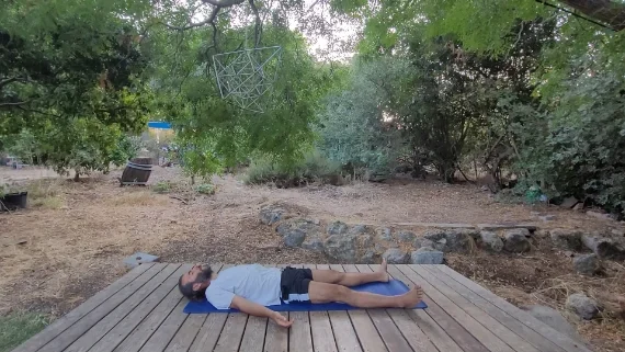 שווהאסנה – תנוחת הרפיה עמוקה גבר שוכב על גבו בתנוחת הרפיה שקטה על מזרן יוגה בלב הטבע