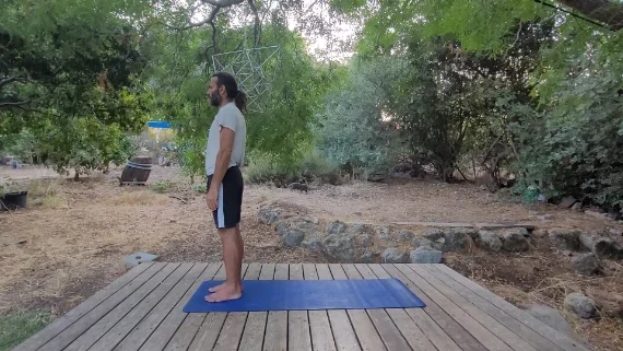 טאדהאסנה – תנוחת עמידה ויציבות גבר עומד זקוף על מזרן יוגה בטבע בתנוחת ההר טאדהאסנה.